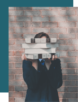 Chica frente a una pared sosteniendo libros ante su cara